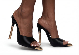 Black high-heeled shoes with gold accents worn by a person on a white background