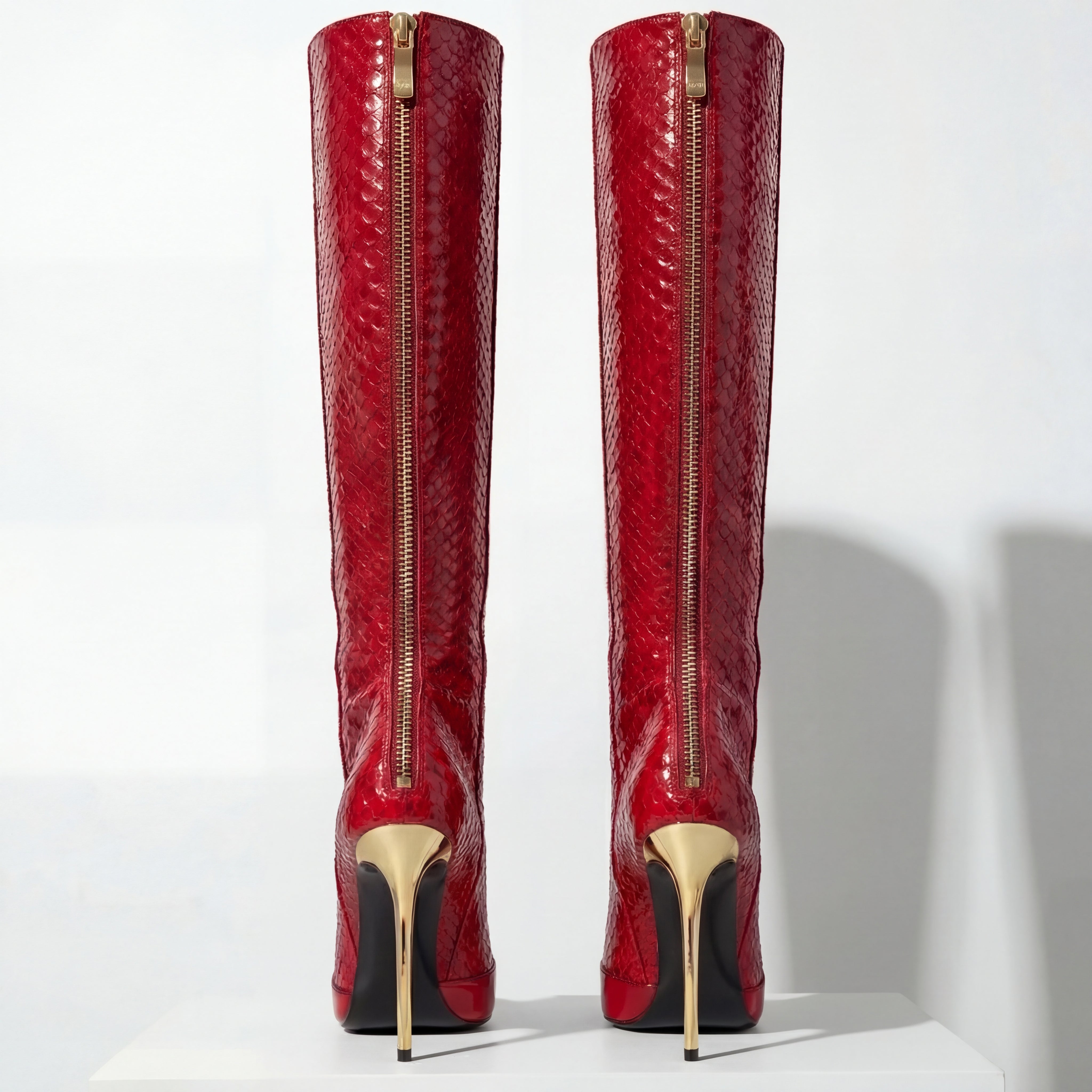 Red knee-high boots with gold zippers and soles on a white background