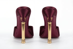 Pair of maroon high-heeled shoes with gold heels on a white background