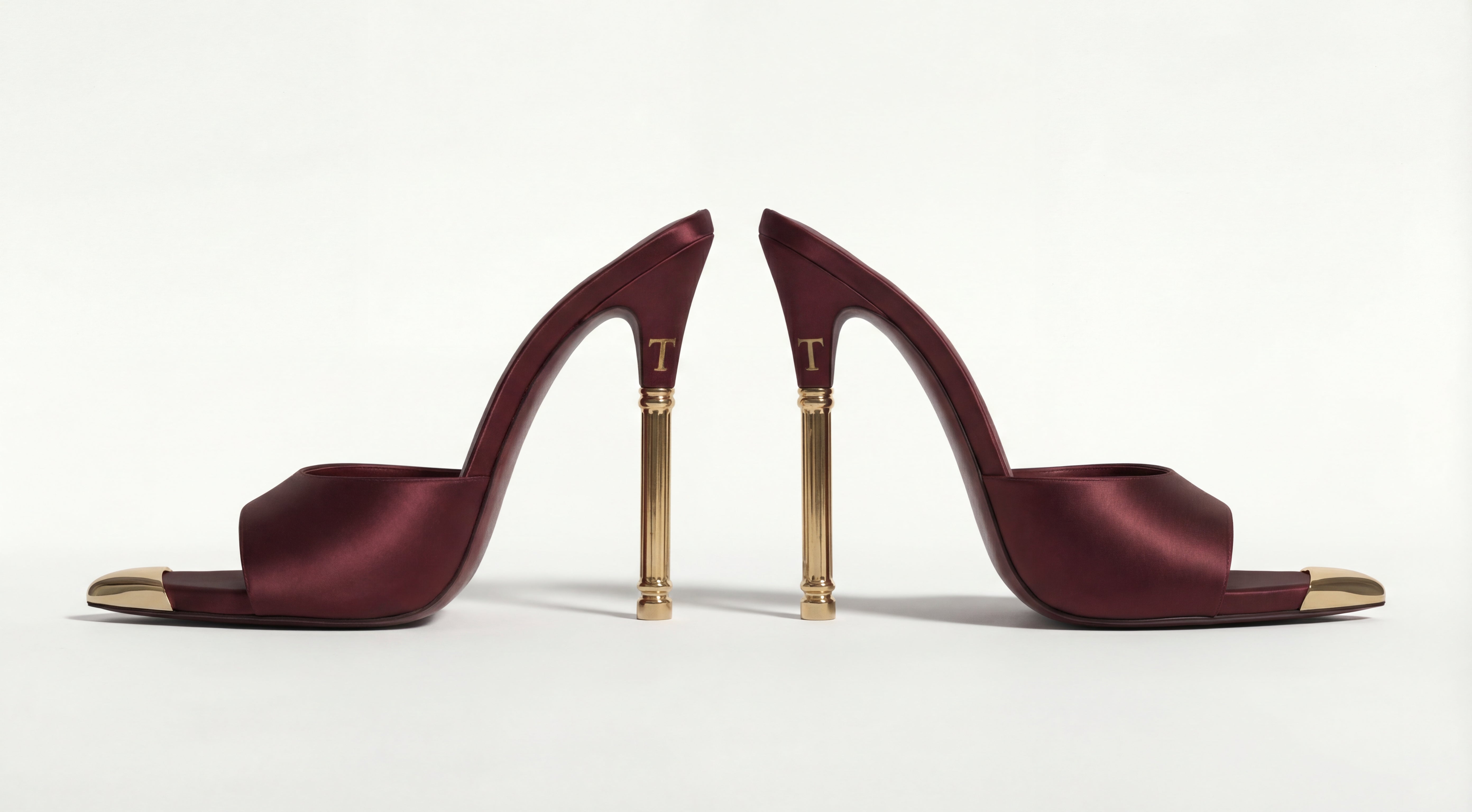 Pair of maroon high-heeled shoes with gold accents on a white background